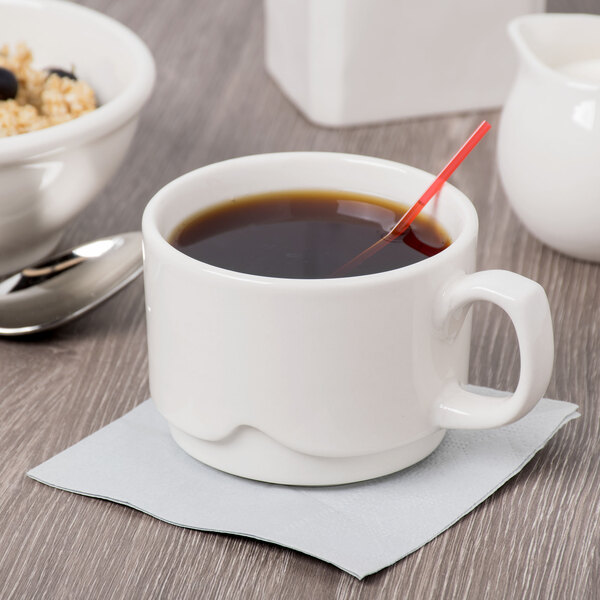 A close-up of a Libbey ivory porcelain large stacking cup of coffee with a spoon.
