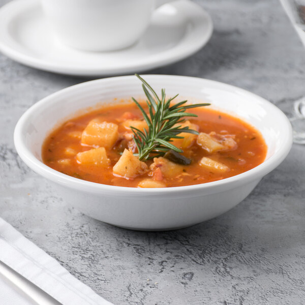 A white Libbey Aluma porcelain bowl filled with soup and a sprig of rosemary.