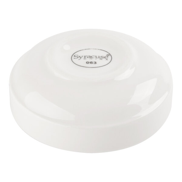 A small, round, white porcelain dish with a slightly raised base and a label on the bottom.