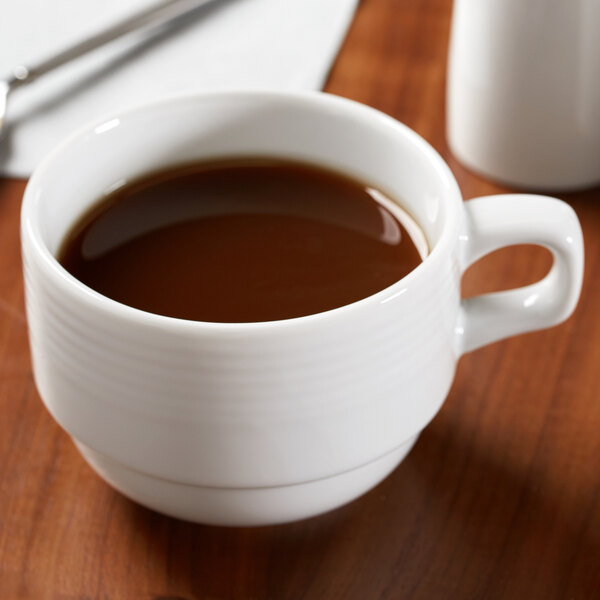 A close-up of a white Libbey Aluma porcelain coffee cup on a table with a cup of coffee and a spoon.