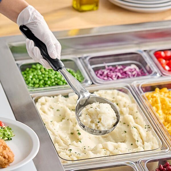 A person using a Vollrath black Jacob's Pride Spoodle to scoop mashed potatoes into a food tray.