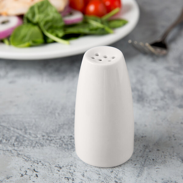 A Libbey ivory porcelain salt shaker next to a plate of salad.