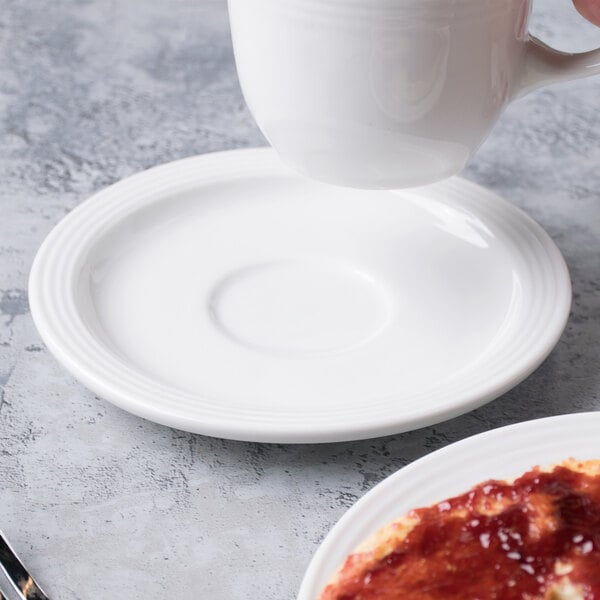 A white Libbey tea saucer under a white cup of coffee on a table with food.