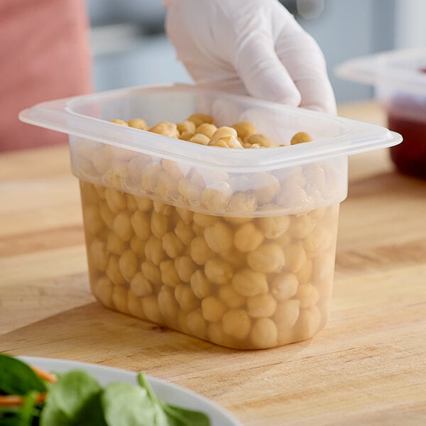 A gloved hand holding a plastic Cambro food container of chickpeas.
