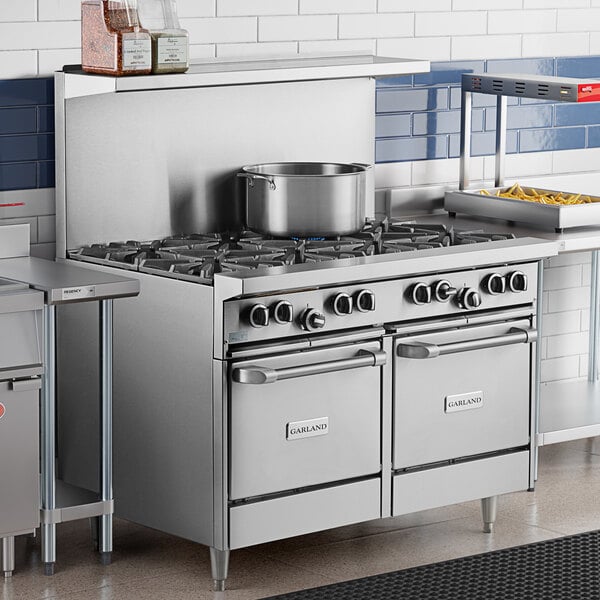 A large stainless steel Garland commercial gas range with two ovens on a counter in a professional kitchen.