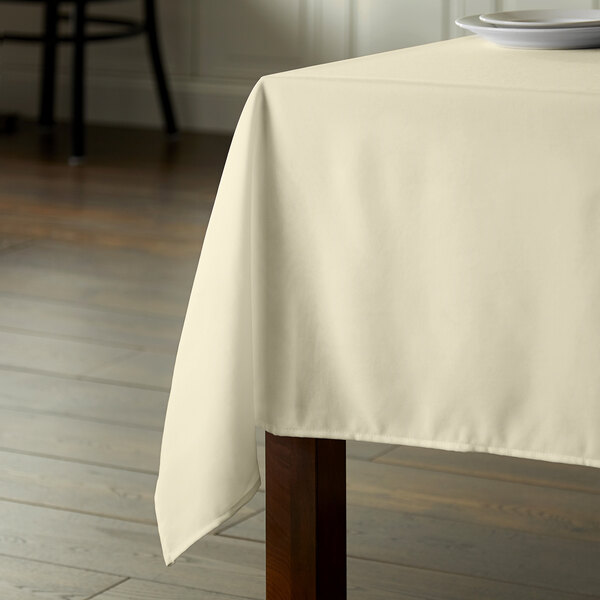 A square wooden table with a white tablecloth on it.