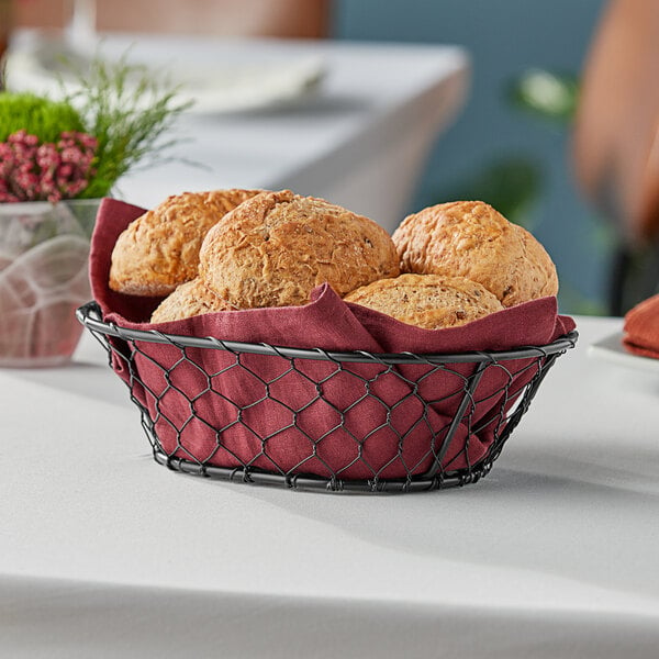 An American Metalcraft black oval chicken wire basket filled with bread on a table.