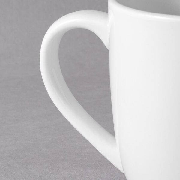 A close-up of a white Tuxton Milano china mug with a handle.