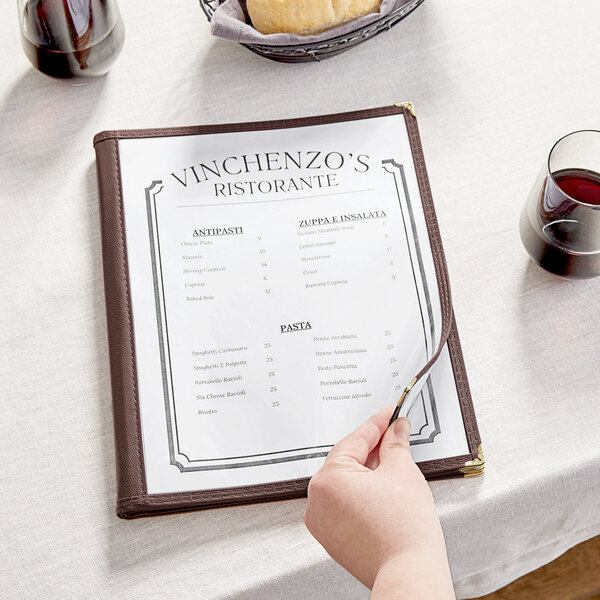 A hand holding a Thunder Group clear menu on a table in an Italian restaurant.