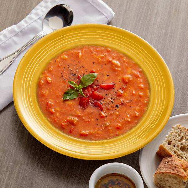 A Tuxton saffron china bowl of soup with a spoon and bread on a table.