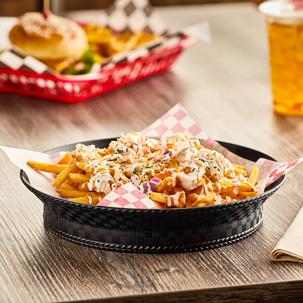 A black Carlisle WeaveWear plastic serving basket filled with french fries on a table.