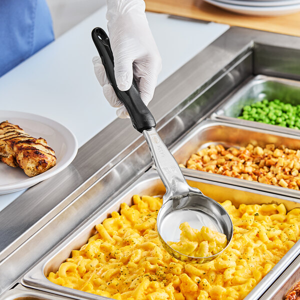 A person holding a Vollrath black solid round spoodle over macaroni and cheese.