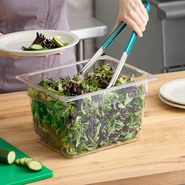 A woman using a green-handled knife to cut salad in a Carlisle clear plastic food pan on a counter.