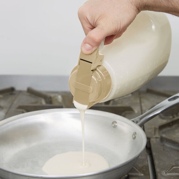 A person pouring milk from a white Tablecraft dispenser into a pan.