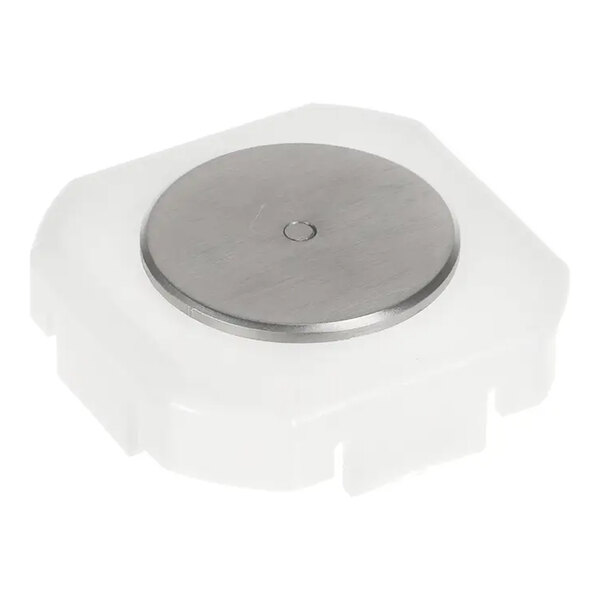 A white plastic component with a circular metallic disc on top, likely a mechanical or electronic part.