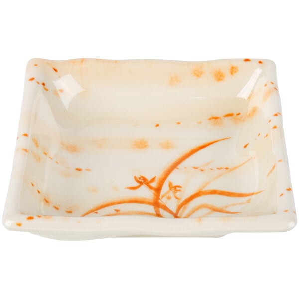A white square bowl with orange floral designs on the inside.