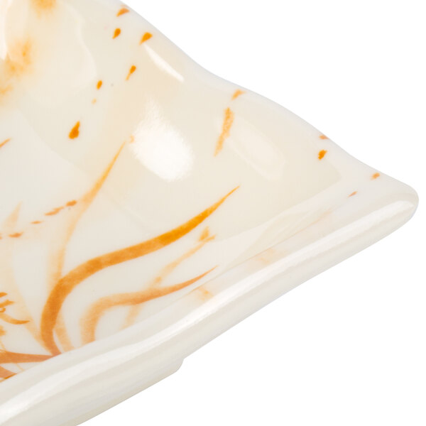 A white square sauce dish with an orange and gold orchid swirl pattern.
