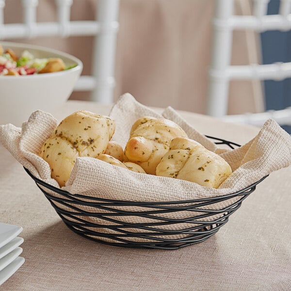 A Tablecraft black wire basket filled with bread rolls on a table.