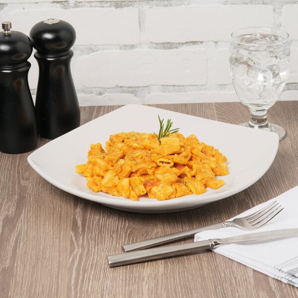 A Libbey ivory porcelain coupe plate with a plate of pasta, a fork, and a knife on it.