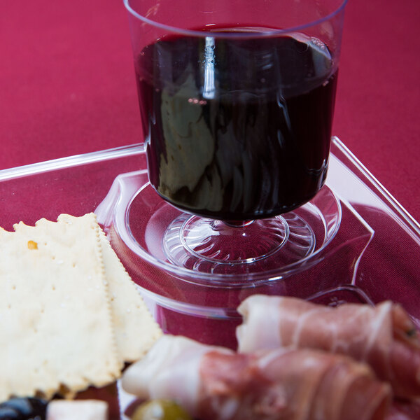 A WNA Comet clear plastic cocktail plate with wine and snacks on it.