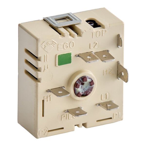 A beige, square-shaped electrical component with multiple metal prongs and labeled terminals, featuring a central adjustment dial and a small green square on its face.