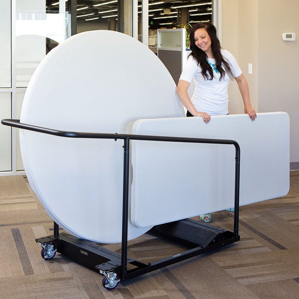 A woman in a white shirt standing next to a large round table on a Lifetime table truck.