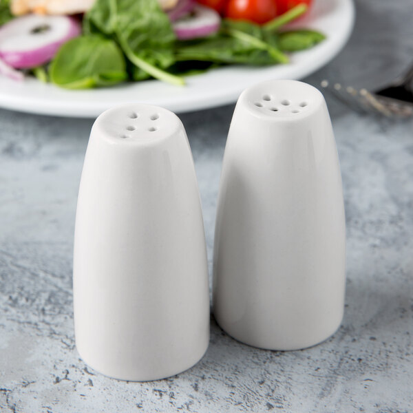 Two Libbey ivory porcelain pepper shakers on a table.