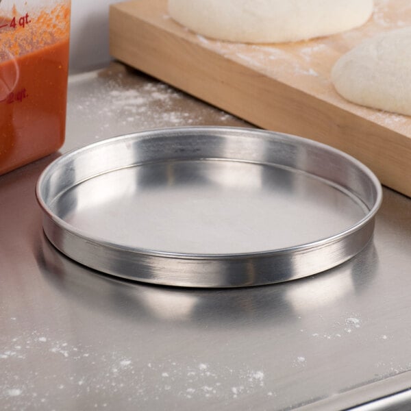 An American Metalcraft aluminum pizza pan with dough on it on a counter.