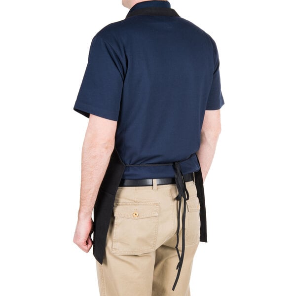 A man wearing a Chef Revival black bib apron with three pockets on a kitchen counter.