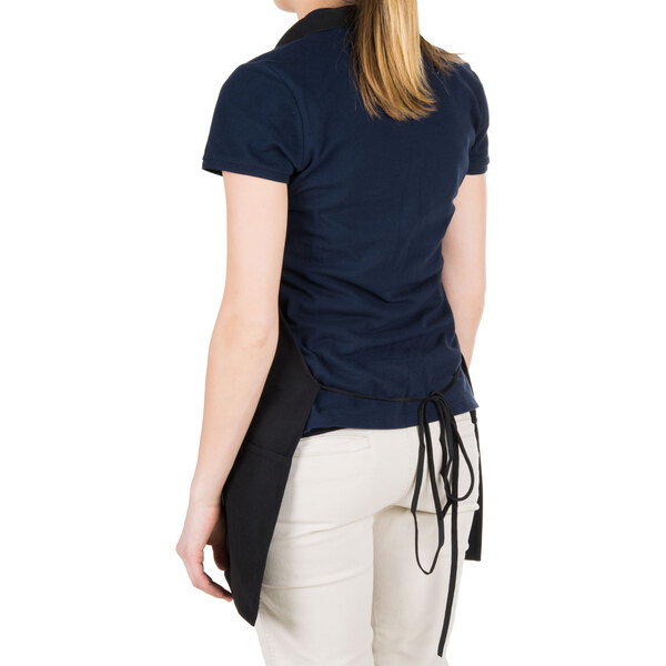 A woman wearing a black Chef Revival bib apron with white pants.