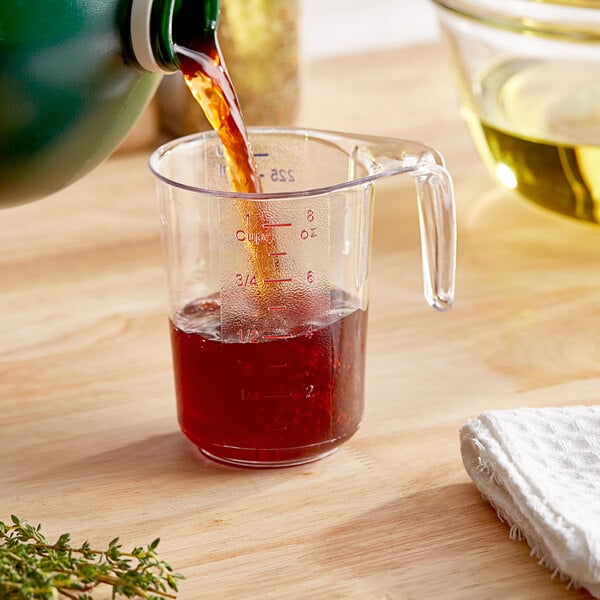 A person pouring liquid into a clear plastic measuring cup.