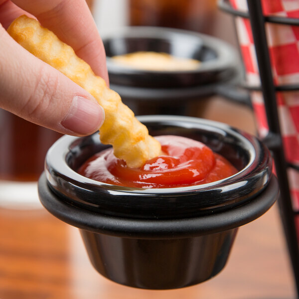 A person dipping a french fry into a Tablecraft black melamine ramekin of sauce.