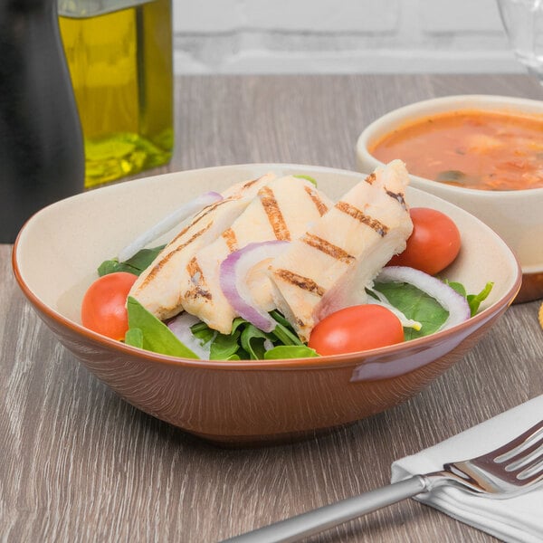 A Libbey terracotta bowl filled with salad with chicken and vegetables on a table.