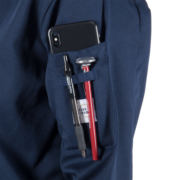 The pocket on a Mercer Culinary Millennia women's navy long sleeve cook jacket holding a phone and pens.