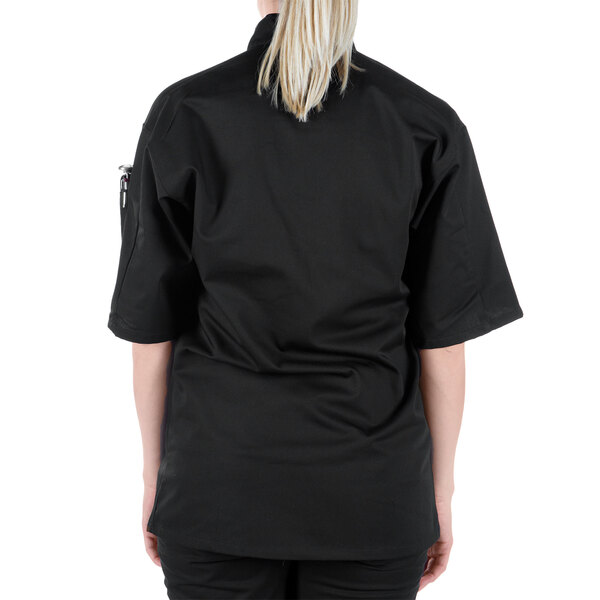 A woman wearing a Mercer Culinary black chef jacket with black cloth buttons.