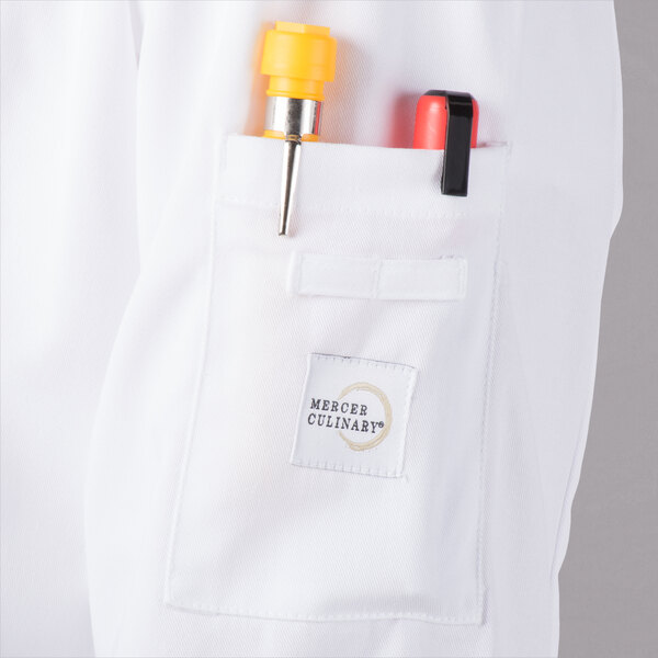 A white Mercer Culinary long sleeve cook jacket with a mesh back and a pocket with a yellow and red pen and a yellow cap.