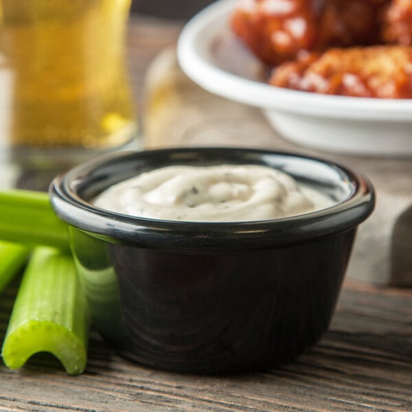 A bowl of white sauce with celery sticks in it placed on a table with wings.