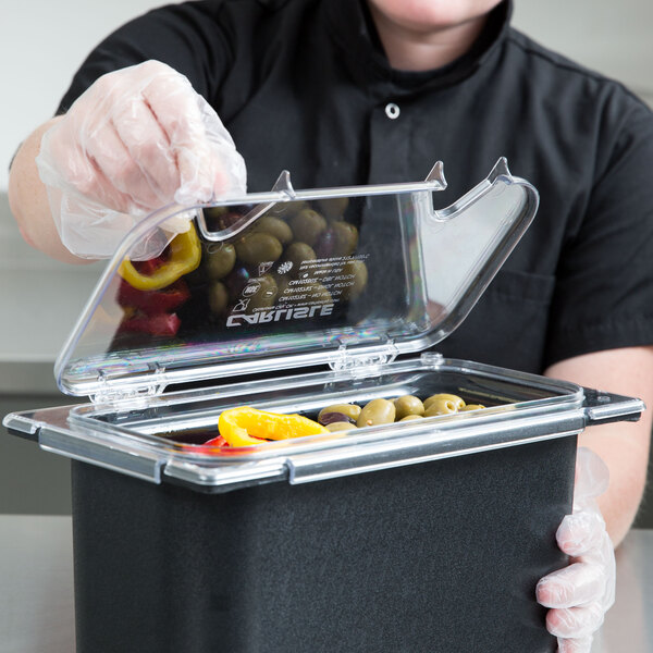 A man in a black shirt holding a Carlisle clear plastic food container lid with a notch over a food container.