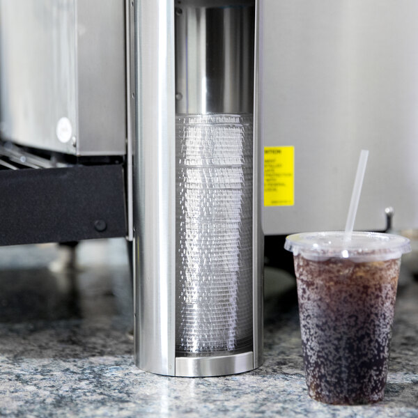 A Vollrath stainless steel lid holder holding lids above a plastic cup of soda on a counter.