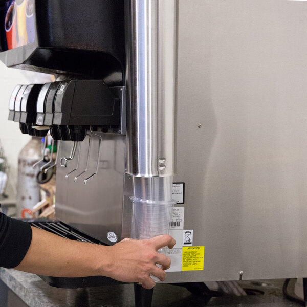 A woman using a Vollrath stainless steel cup dispenser on a countertop to fill a plastic cup.