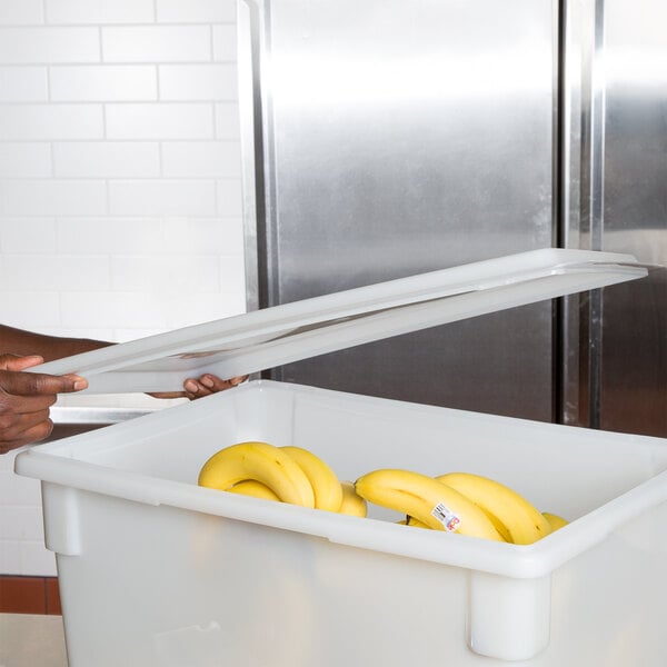 A person using a Carlisle food storage lid to hold a bunch of bananas.