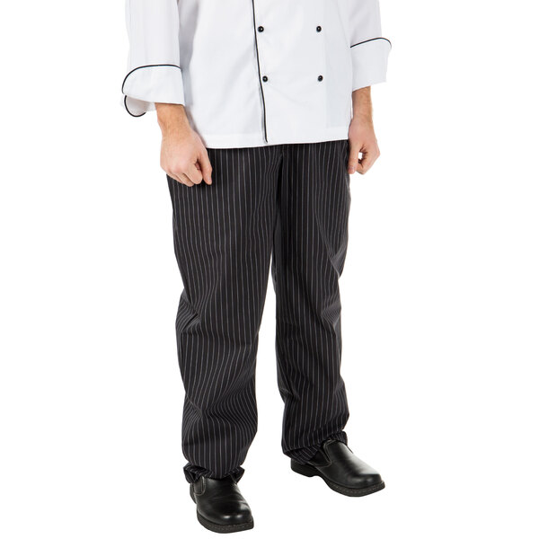 A person wearing Mercer Culinary Millennia black pinstriped cook pants on a counter in a professional kitchen.