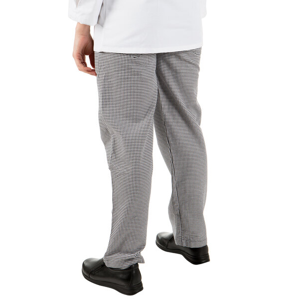 A person wearing Mercer Culinary houndstooth chef pants with their hands in their pockets.