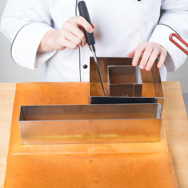 A person using a Matfer Bourgeat square cake frame to cut a cake.