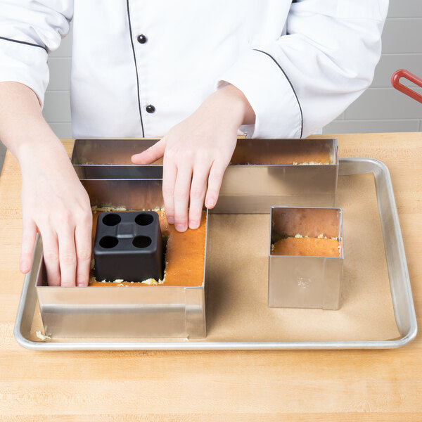 A person in a chef's uniform cutting a cake with a Matfer Bourgeat square cake frame.