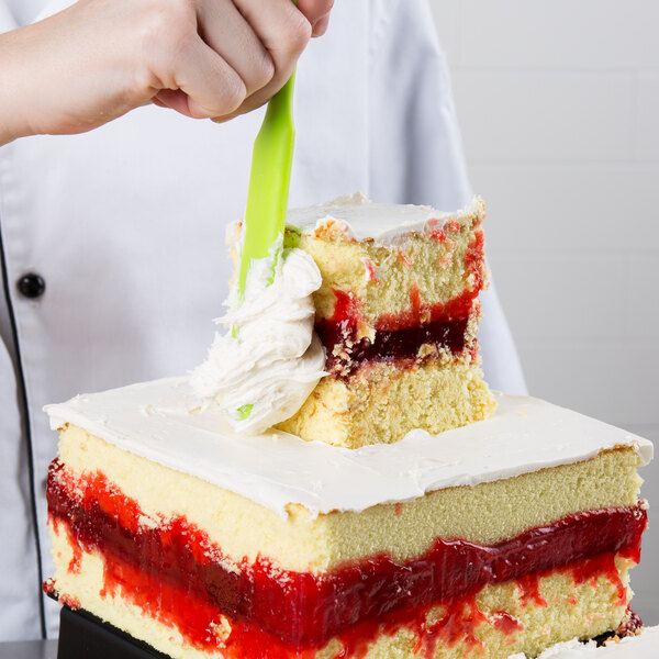 A person cutting a square cake with a strawberry jelly on top.