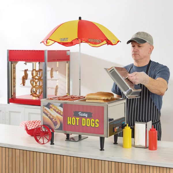 A small countertop hot dog cart with a red and yellow umbrella, labeled 'Tasty Hot Dogs,' designed for holding and serving hot dogs and buns.
