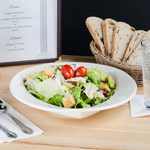 A bowl of salad with tomatoes and croutons on a table with a glass of water.