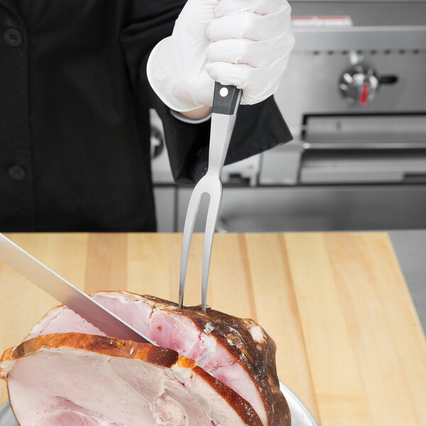 A person using a Mercer Culinary Renaissance forged carving fork to cut a ham.