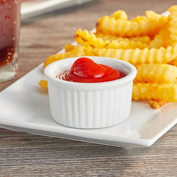 A plate of french fries with ketchup served in Acopa bright white fluted porcelain ramekins.